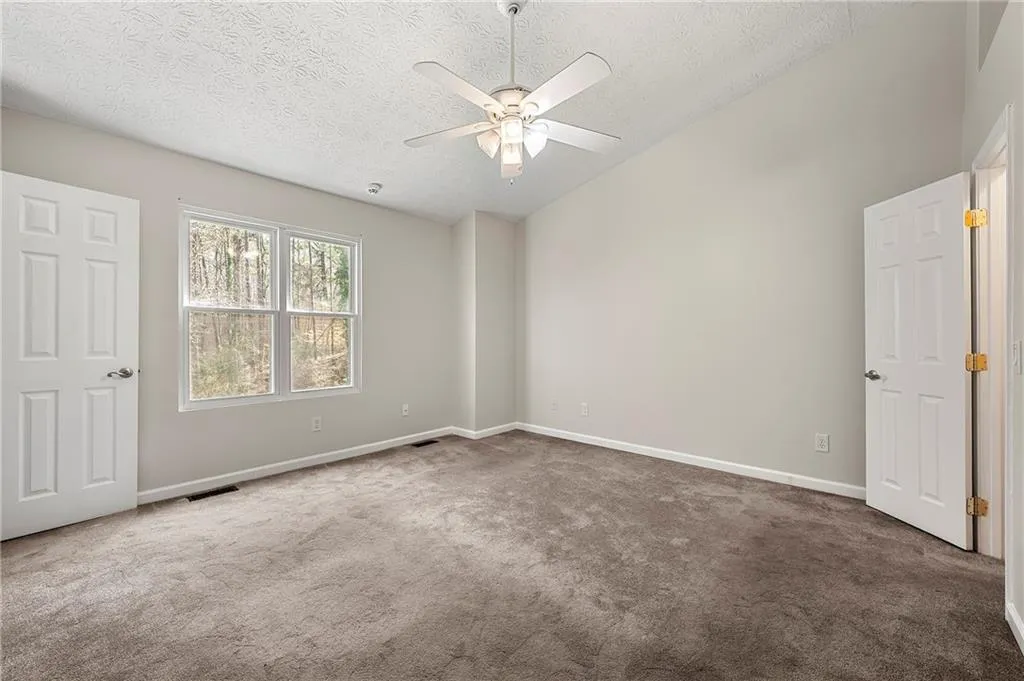 Carpeted empty room with lofted ceiling, baseboards, visible vents, and a textured ceiling