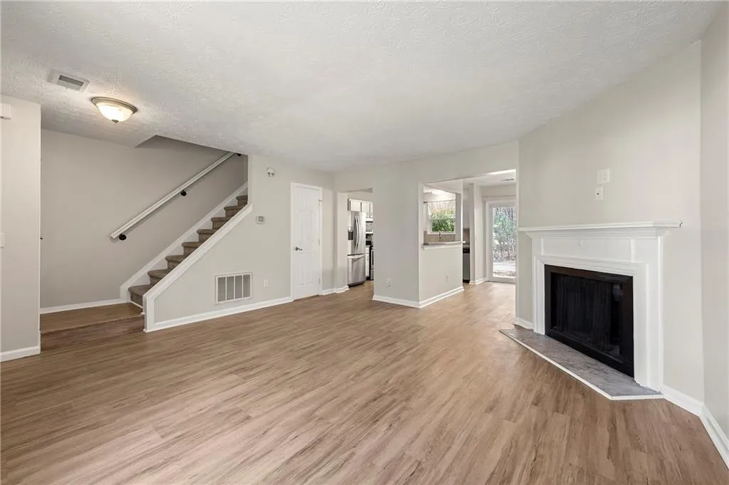 Unfurnished living room featuring light wood-type flooring, stairway, visible vents, and a fireplace with raised hearth