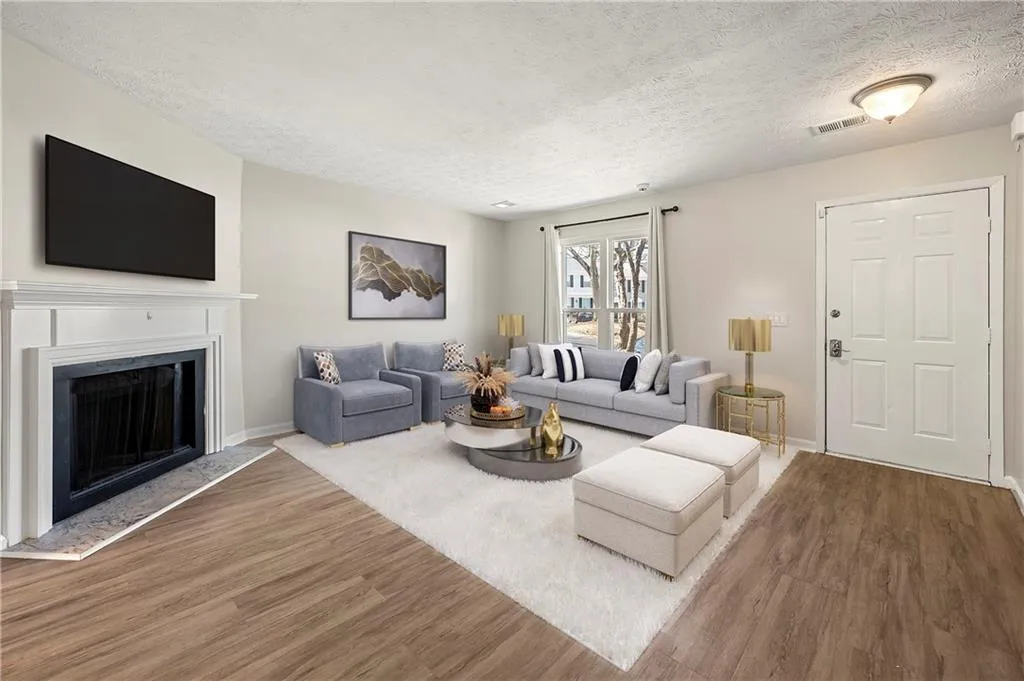 Living room with a fireplace with raised hearth, a textured ceiling, wood finished floors, visible vents, and baseboards