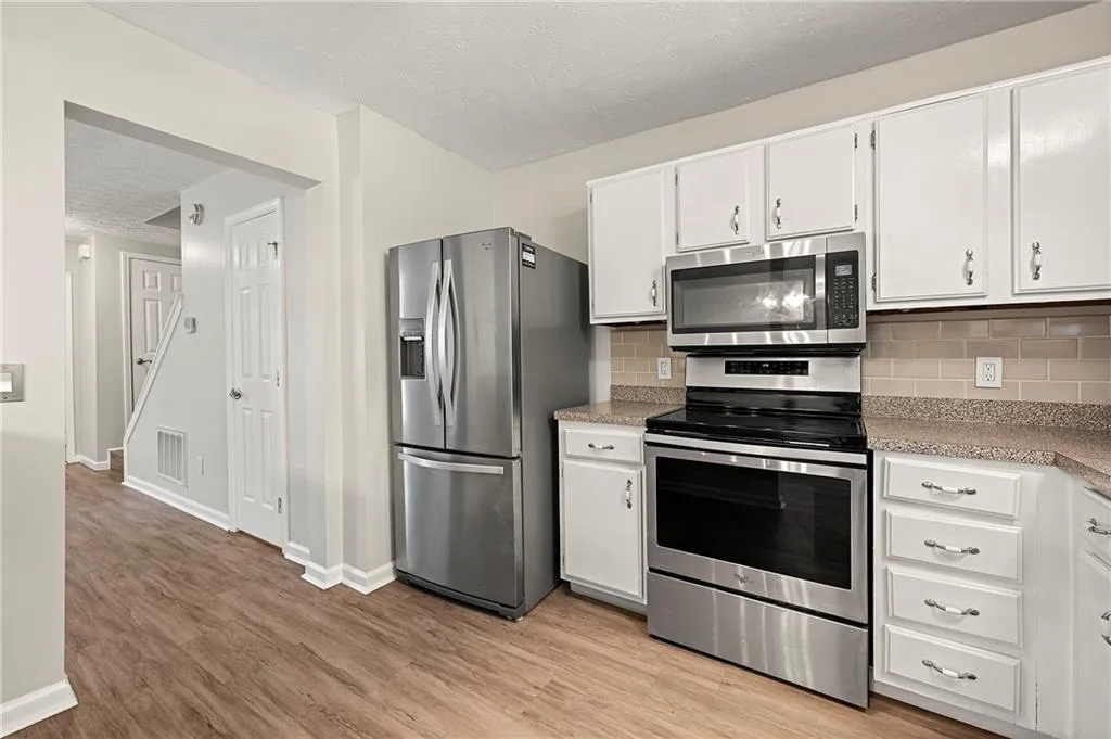 Kitchen with light wood finished floors, stainless steel appliances, tasteful backsplash, visible vents, and white cabinetry