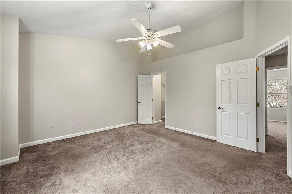 Unfurnished bedroom with carpet floors, high vaulted ceiling, baseboards, and a textured ceiling