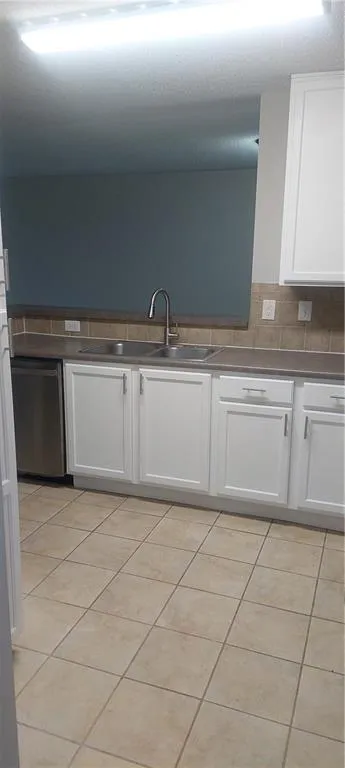 Kitchen with white cabinets, dark countertops, light tile patterned flooring, and dishwasher