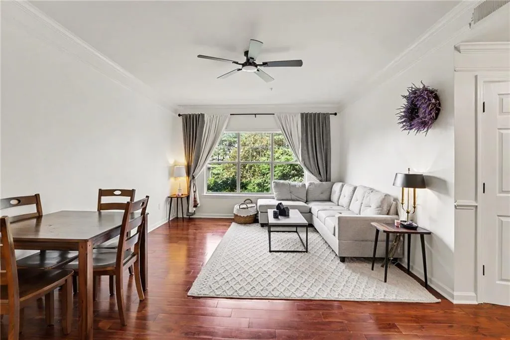 Expansive living space featuring wood-finish flooring, white walls, and a large window with outdoor greenery