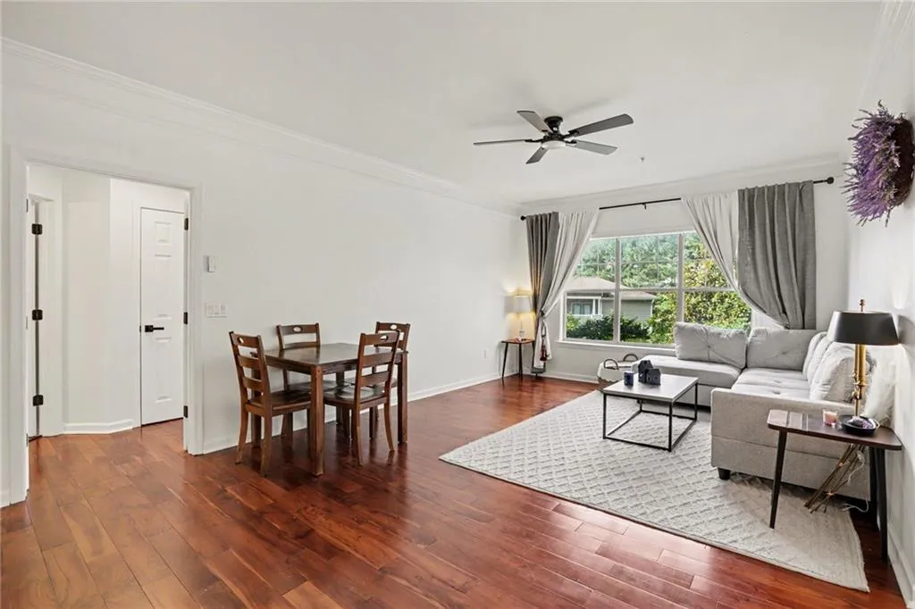 Open-concept living area featuring wood-finish flooring, a contemporary ceiling fan, large windows, crown molding, and a spacious layout
