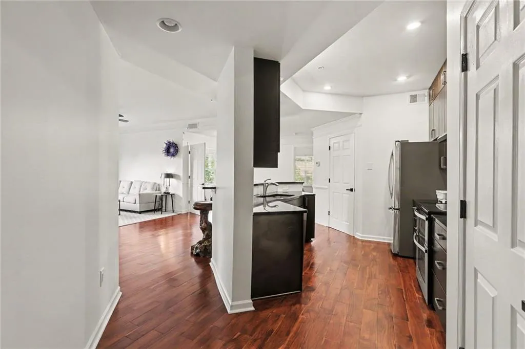 Kitchen area featuring rich wood-finish flooring, recessed lighting, stainless steel appliances, dark cabinetry, and a sleek sink with a pull-down faucet