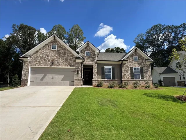 Stone and brick facade with dark shutters, gabled roofline, concrete driveway, and attached two-car garage