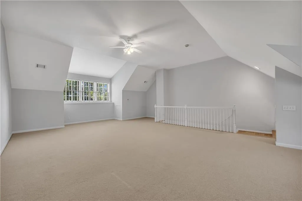 Vaulted ceiling with an attached ceiling fan, multiple windows with white sills, neutral carpeting, and a white railing
