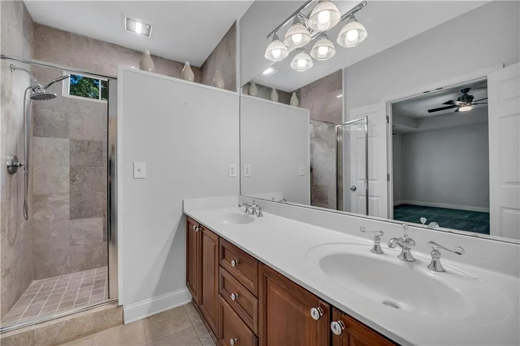 Spacious bathroom featuring a dual vanity, polished chrome fixtures, integrated sinks, a walk-in shower with glass enclosure, and tiled walls