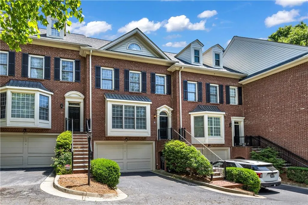 Brick townhouse facade with bay windows, black shutters, and integrated two-car garage
