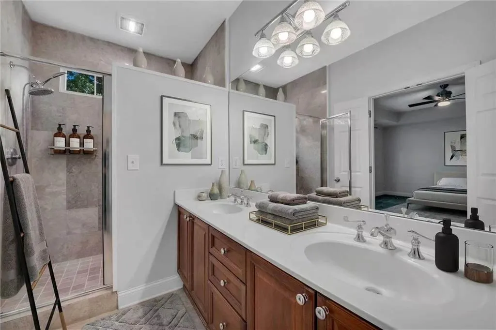 Dual-sink vanity with wood-finish cabinetry, white countertop, and extensive mirrored wall