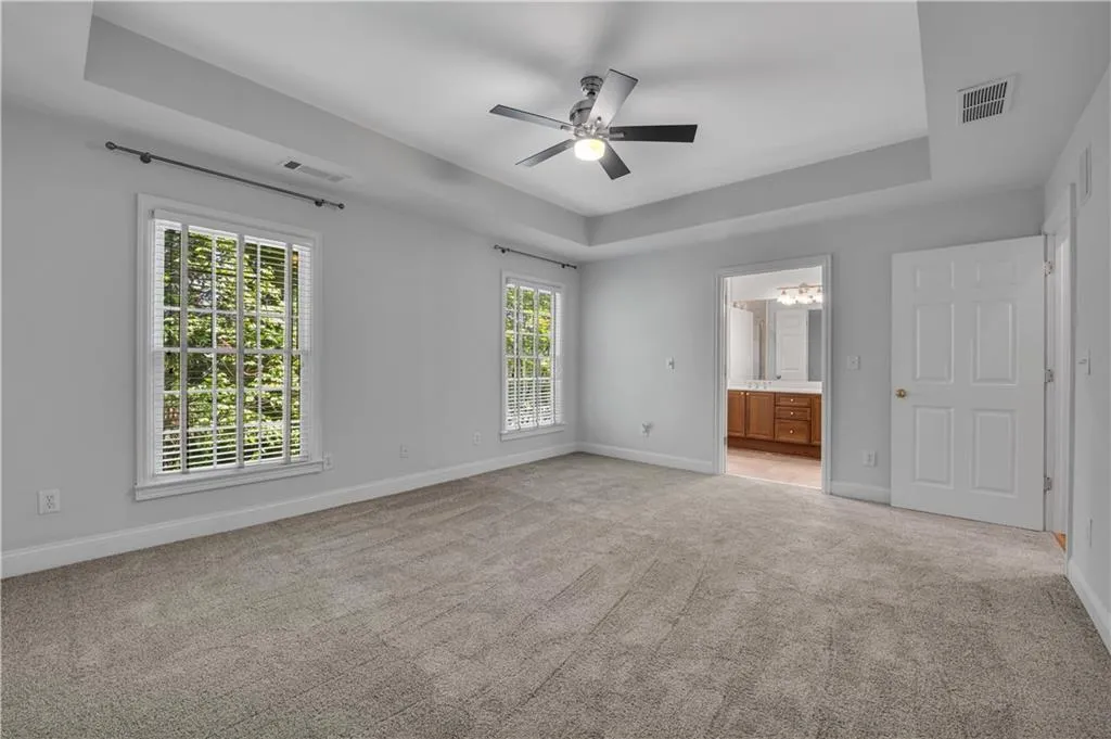 Tray ceiling with a ceiling fan, two windows with blinds, and neutral carpeting