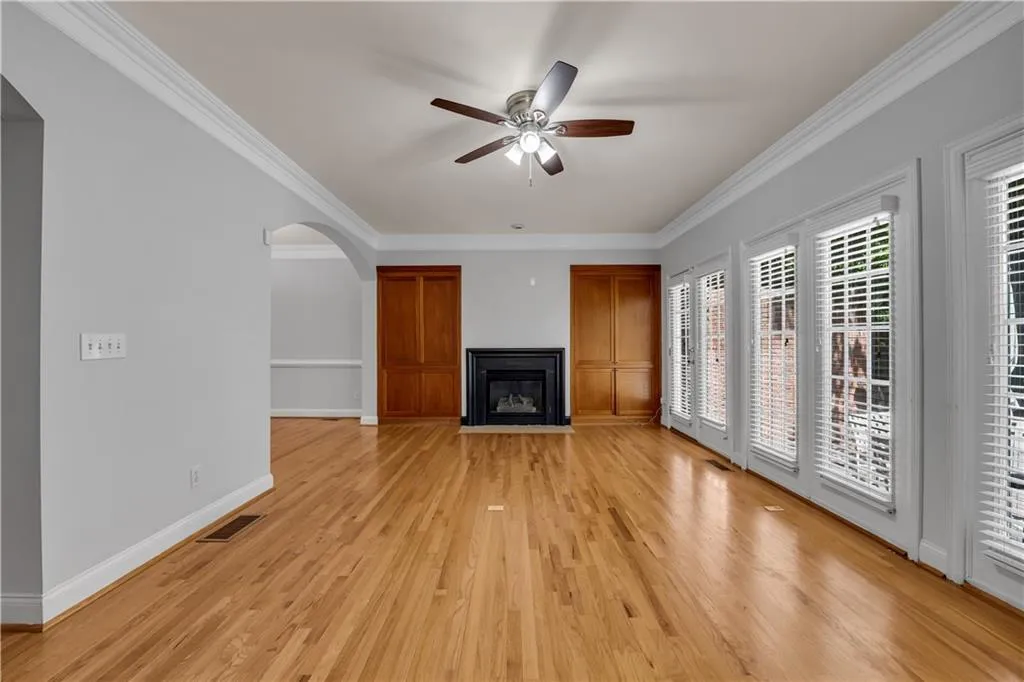 Hardwood flooring throughout, crown molding, arched doorway, built-in cabinetry, and a fireplace with a black surround