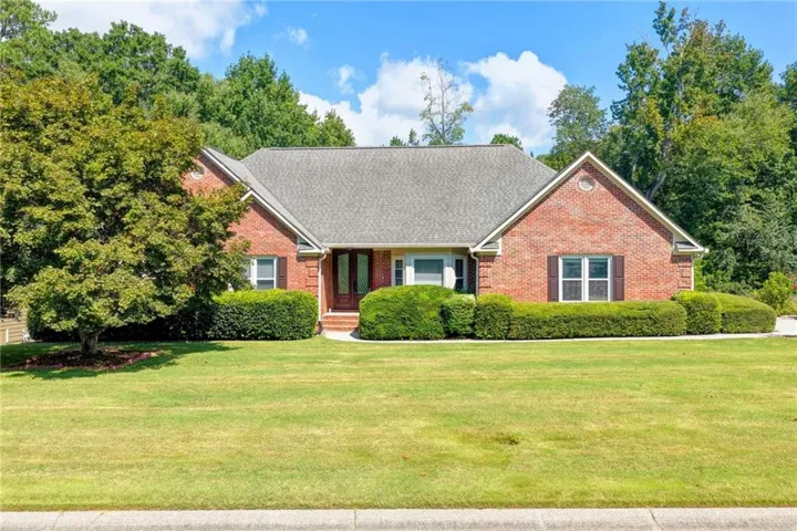 Brick facade residence with a gabled roofline, mature landscaping, wood-finish front entry, and shuttered windows