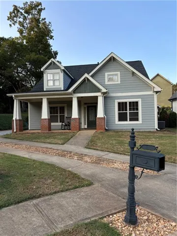 Light blue siding exterior with a dark shingle roof, featuring a covered front porch with white columns and brick bases, a decorative black mailbox on a stone bed, and a concrete pathway