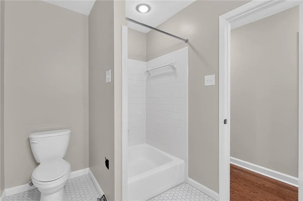 White hexagonal floor tiles, white subway tile shower surround, white bathtub, recessed ceiling lighting, and a white toilet
