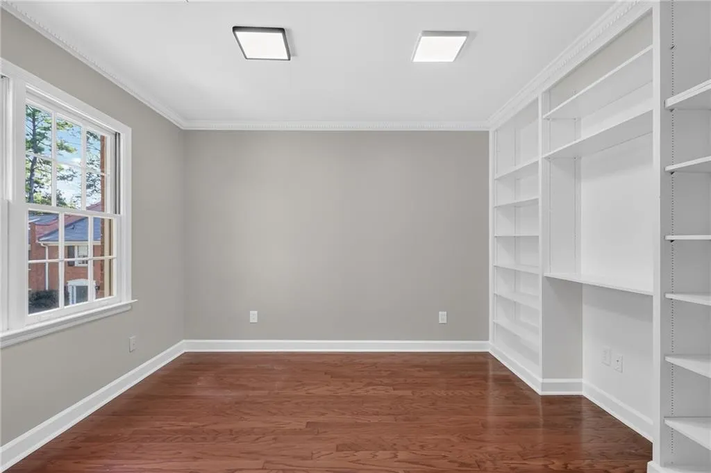Built-in shelving, hardwood flooring, crown molding, white trim, and square flush-mount lighting fixtures