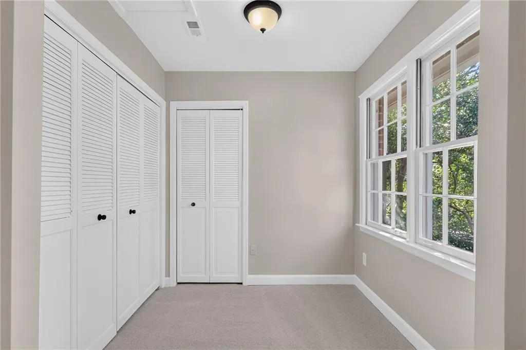 Neutral wall finishes, white trim, multiple louvered bifold doors, double-hung windows, and plush carpet flooring