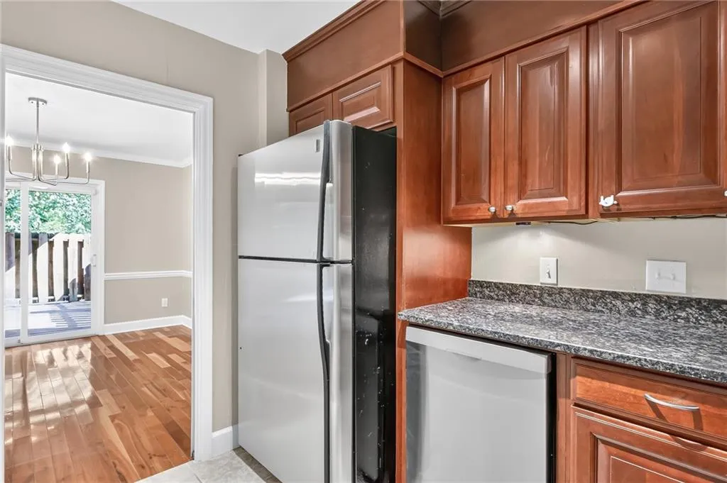 Cherry wood cabinetry, stainless steel refrigerator, dark speckled countertops, integrated dishwasher, and under-cabinet lighting
