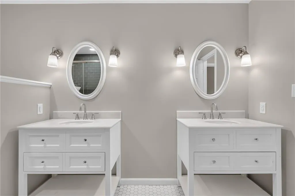 Dual white vanity cabinets with integrated sinks, brushed nickel fixtures, oval mirrors, and sconce lighting
