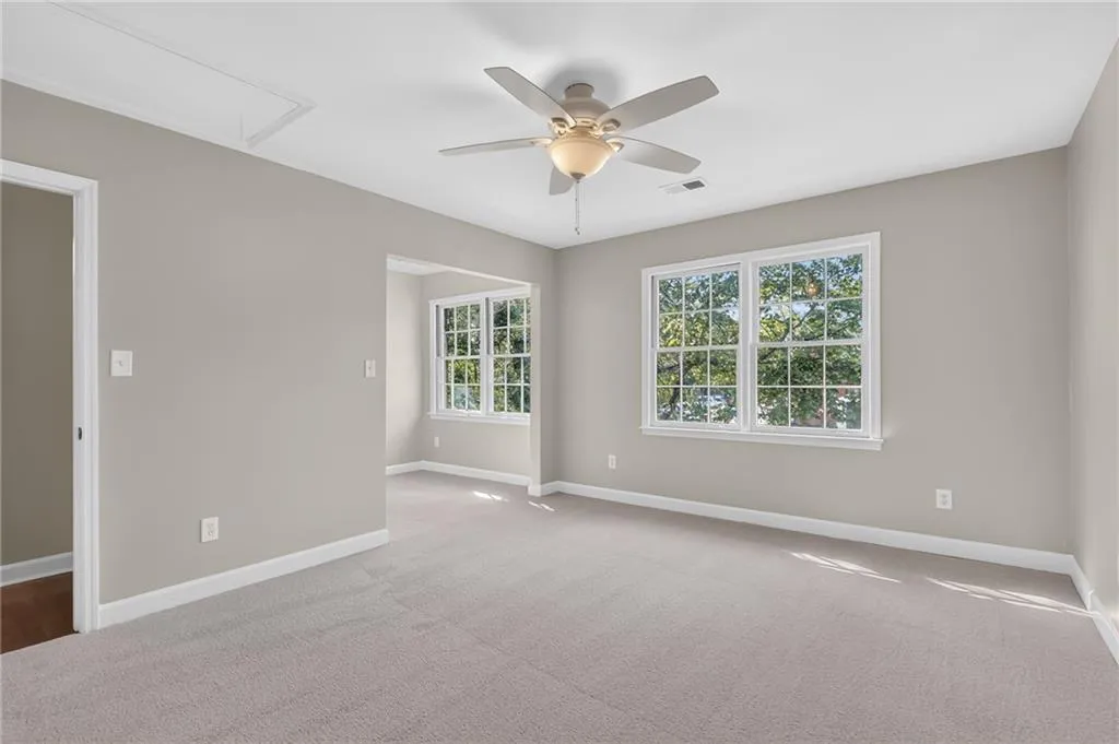 Carpeted room with a ceiling fan, light-colored walls, and multiple windows