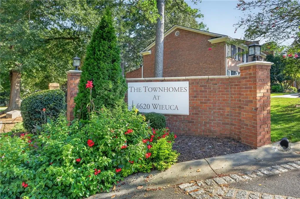 Brick entrance wall with stone caps, integrated light fixture, and lush landscaping