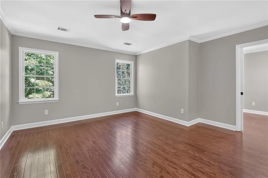 Hardwood flooring, painted walls, crown molding, white trim, and a ceiling fan with integrated lighting