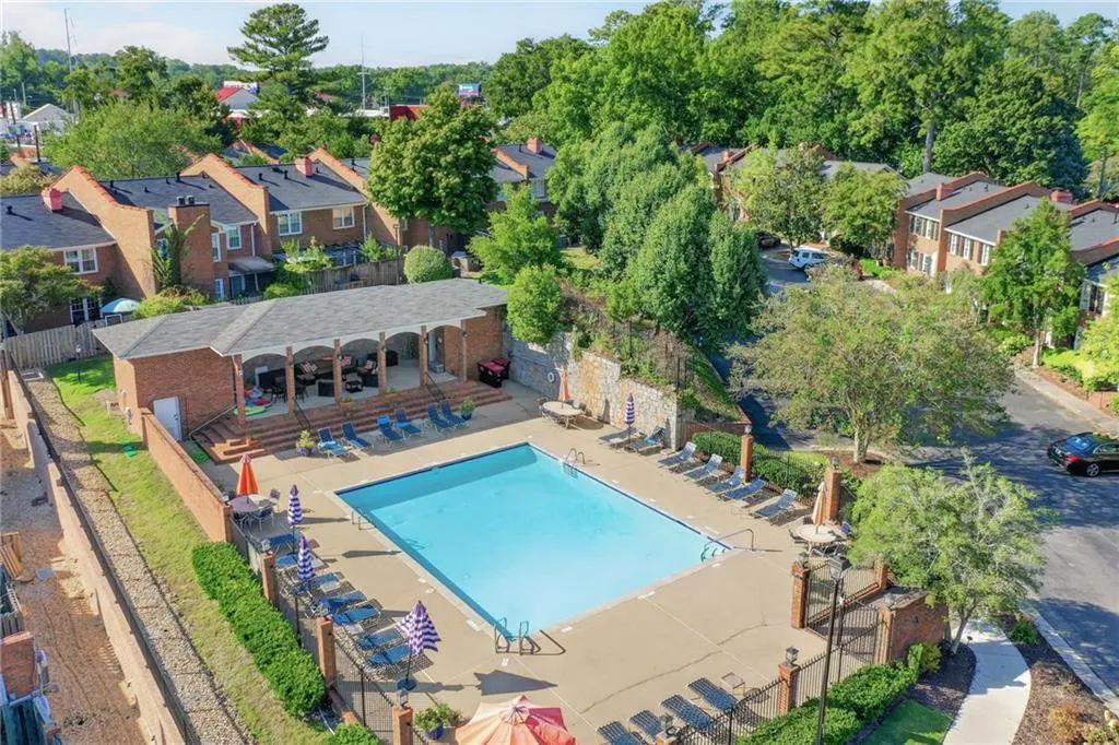 Rectangular swimming pool with surrounding lounge area, brick-clad pool house with arched entryways, and mature landscaping