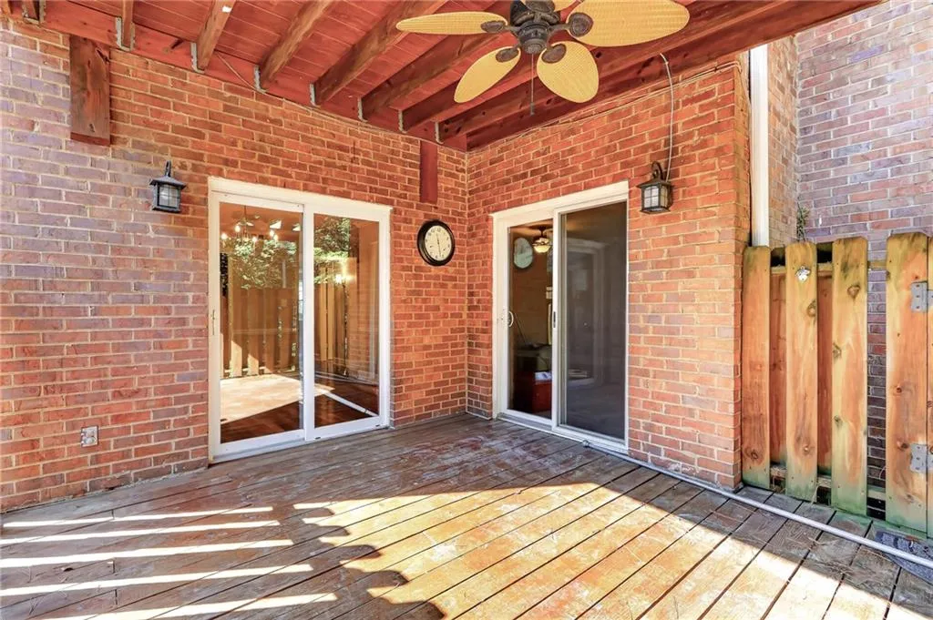 Covered outdoor deck featuring exposed wood beams, a ceiling fan, and brick exterior walls