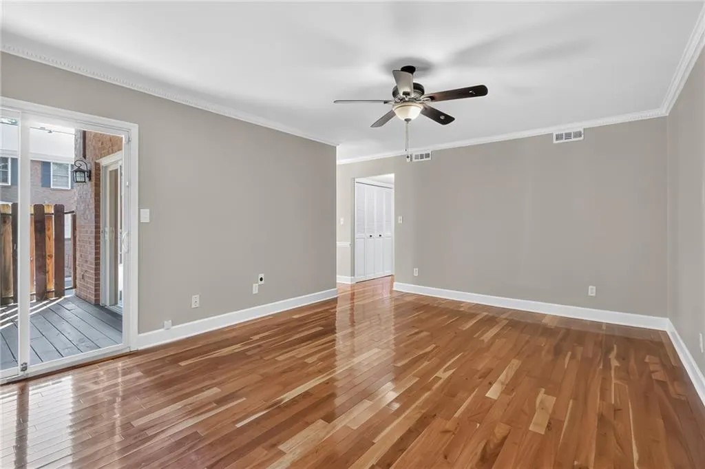 Wood-finish flooring, crown molding, ceiling fan with integrated lighting, neutral wall palette, and sliding glass door to a private deck