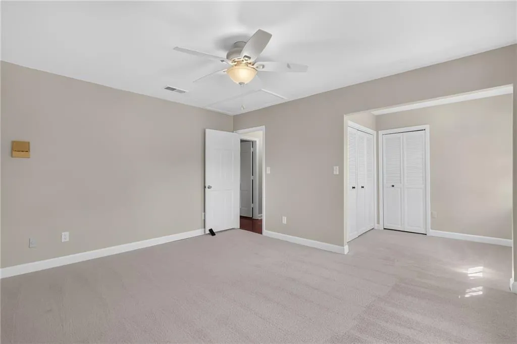 Neutral tone wall paint, white trim, ceiling fan with integrated lighting, two bi-fold louvered doors, and light-colored carpeting