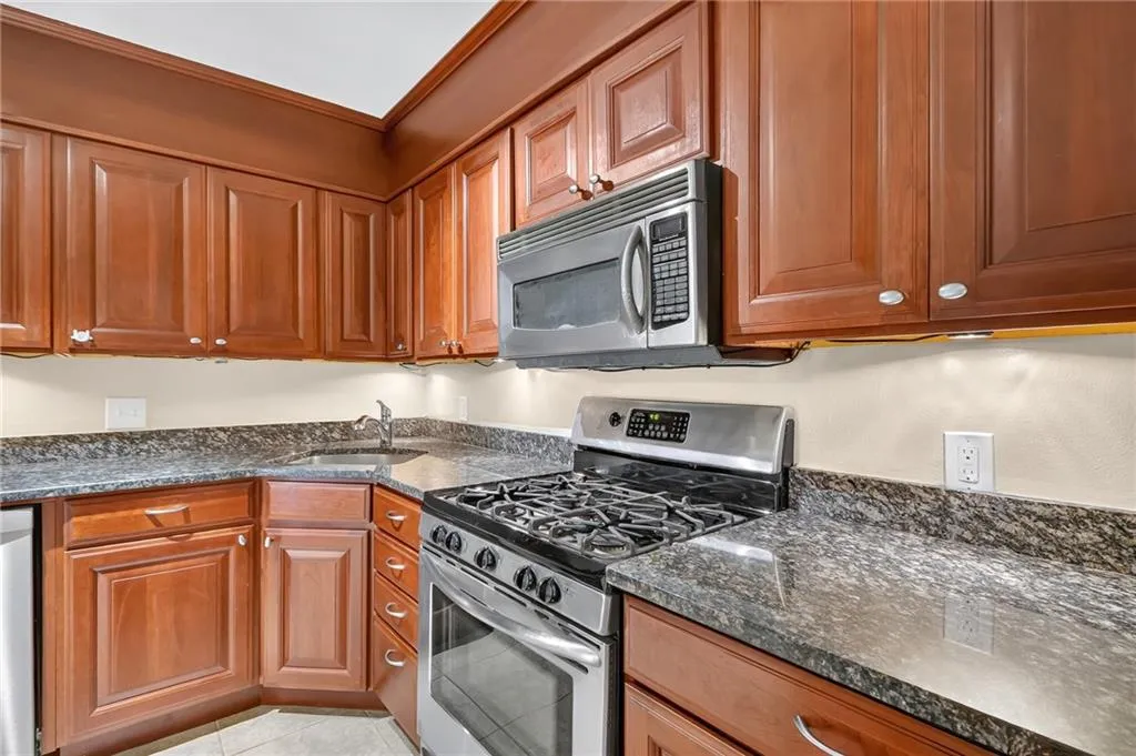 Rich wood-finish cabinetry, stainless steel oven with gas cooktop, stainless steel microwave, and stone-finish countertops