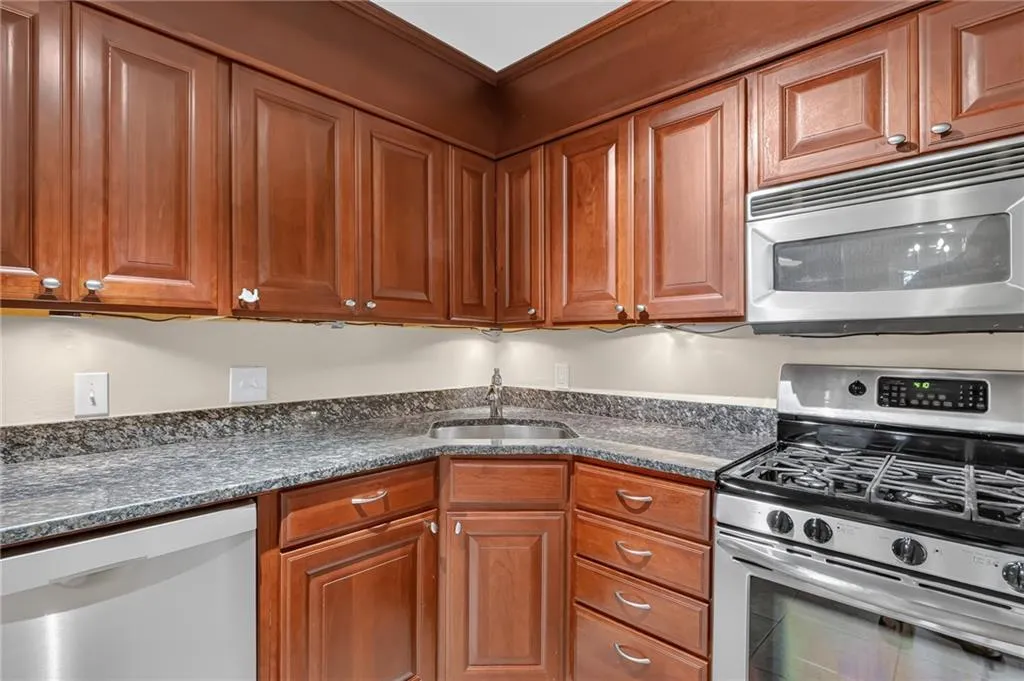 Kitchen featuring wood cabinetry, stainless steel microwave, stainless steel gas range, stainless steel dishwasher, and a stainless steel sink