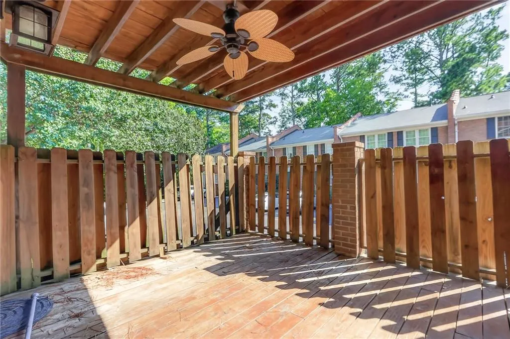 Expansive wooden deck featuring a slatted privacy fence, a wood-slatted pergola, an attached ceiling fan, and an exterior light fixture