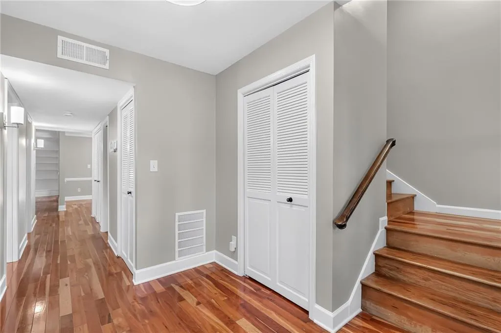 Hardwood flooring throughout, white baseboards, louvered bi-fold doors, wood staircase with dark handrail, and flush-mounted ceiling lighting
