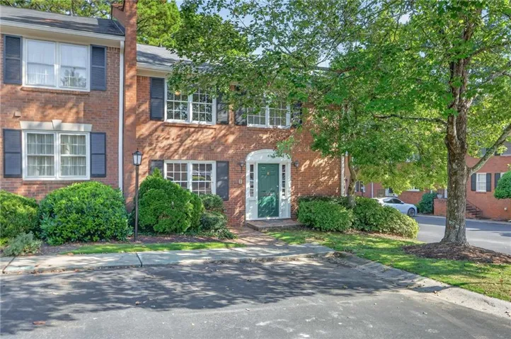 Brick exterior, white window trim, dark shutters, covered front entry, and mature landscaping