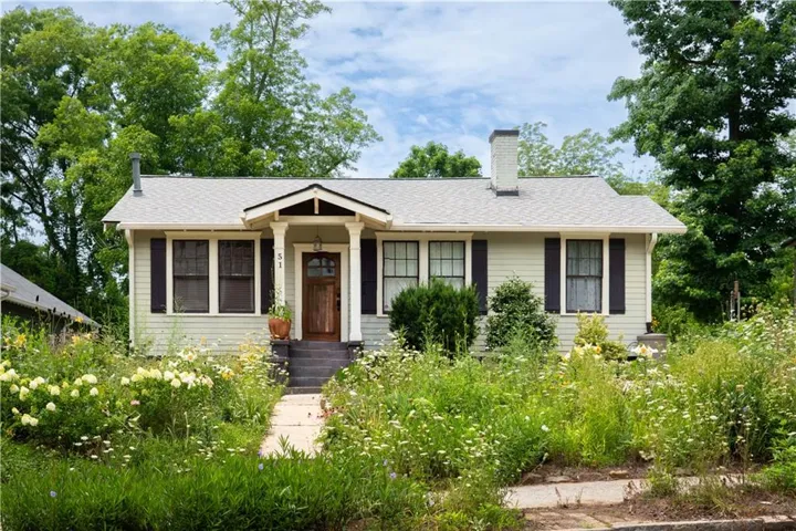 Craftsman-style home featuring light-toned siding, a covered entry porch, and dark louvered shutters