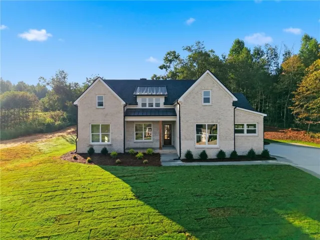 Light-colored brick facade with a dark shingle roof, featuring a covered entry with wood accents and a paved driveway