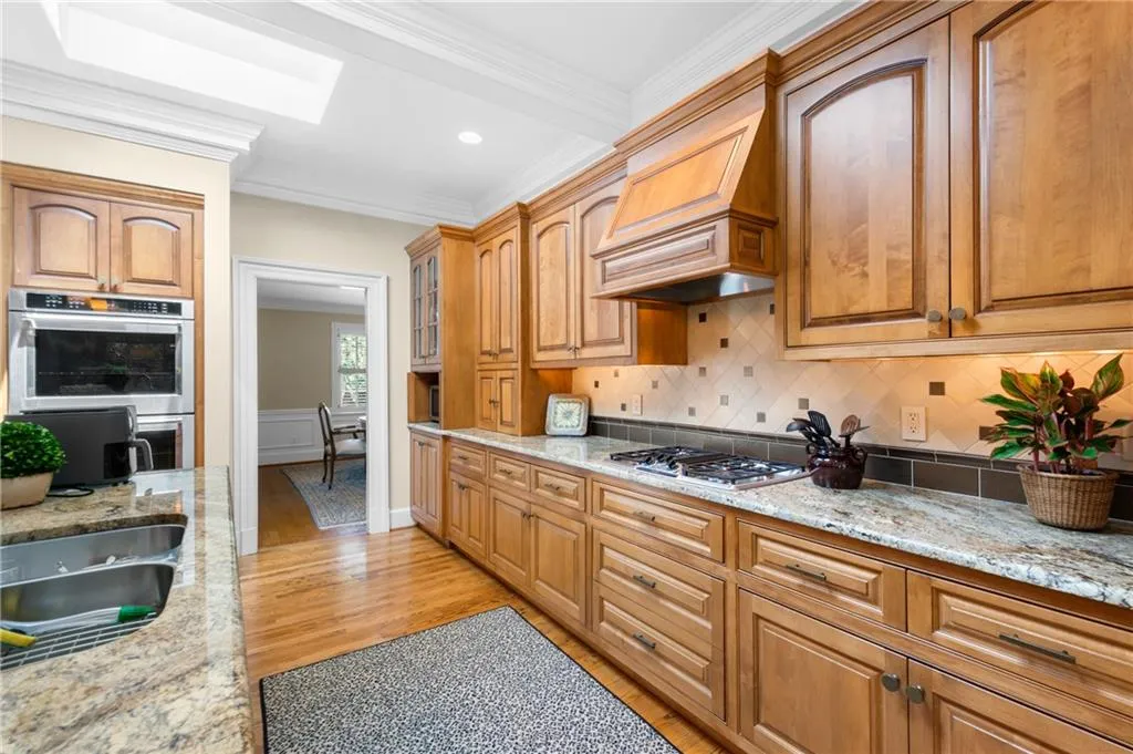 Kitchen featuring custom exhaust hood, stainless steel appliances, decorative backsplash, ornamental molding, and light hardwood flooring