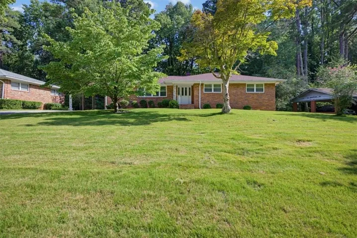 Brick exterior residence with a front lawn, mature trees, and a detached carport