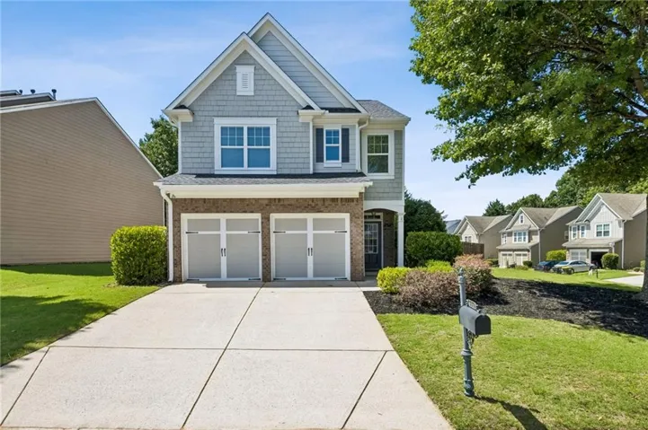 Two-story residence featuring light gray siding, brick accents, and a two-car garage