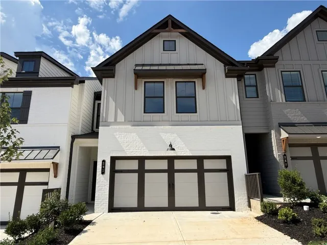 Contemporary townhome with board and batten siding, white brick facade, dark trim details, and a dark paneled garage door