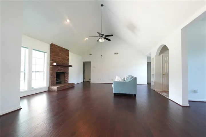 Vaulted ceiling, brick fireplace with wood mantle, dark wood-finish flooring, recessed lighting, and arched doorway