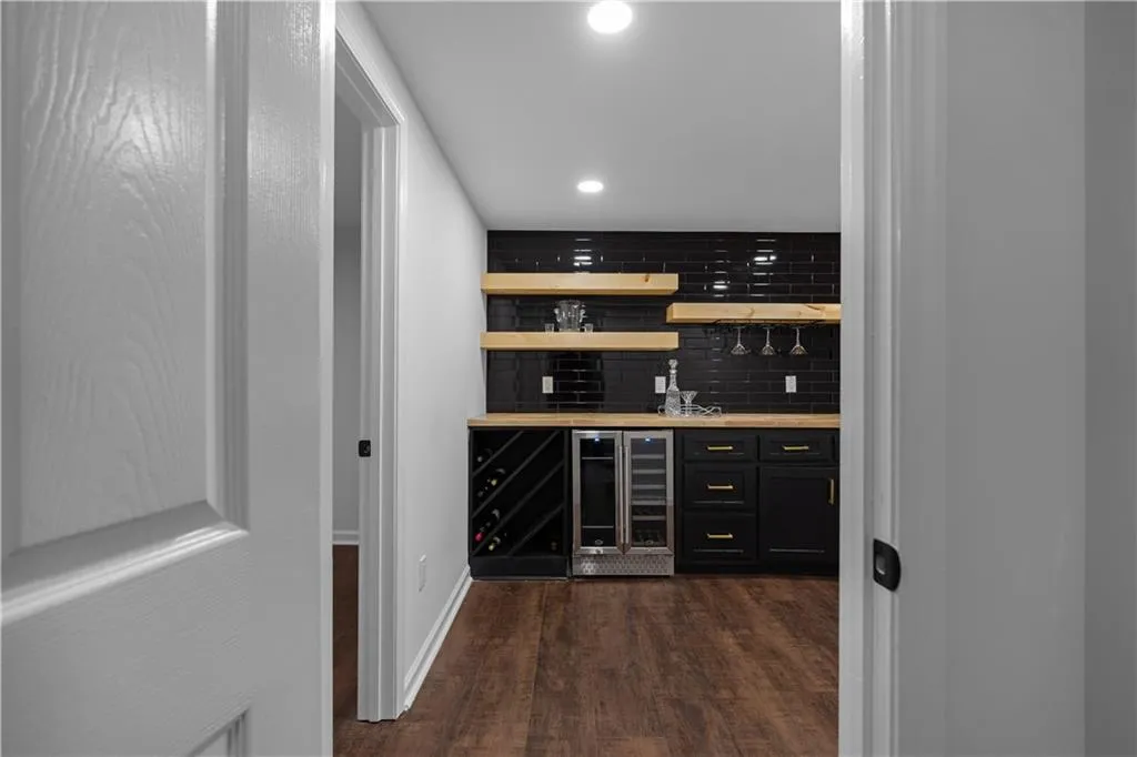 Bar with dark wood-type flooring, beverage cooler, and backsplash