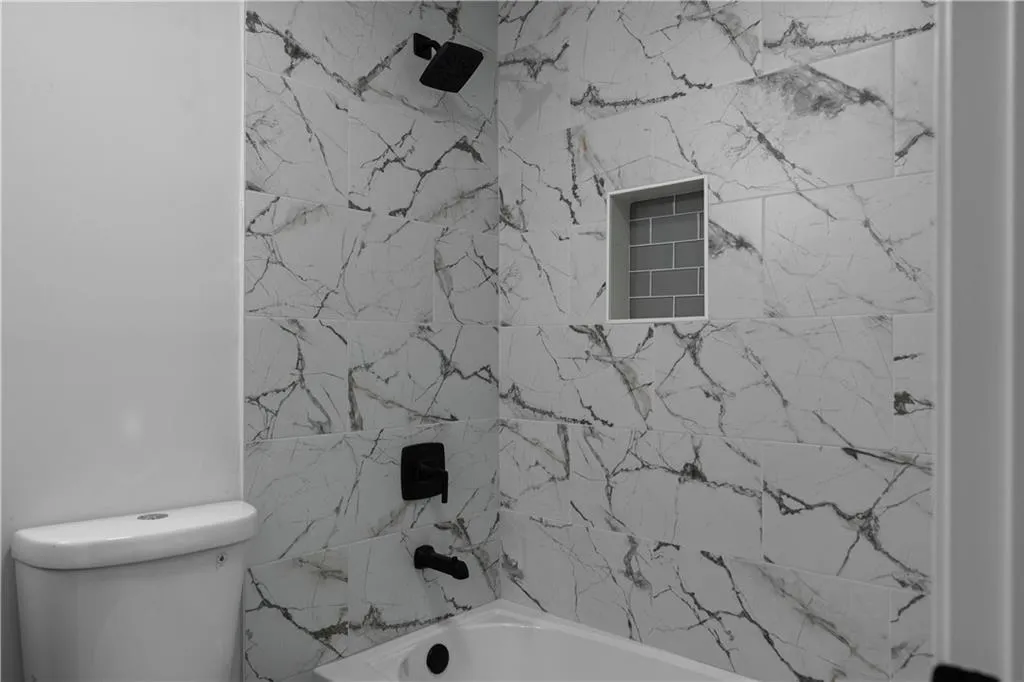 Bathroom with tiled shower / bath combo and toilet