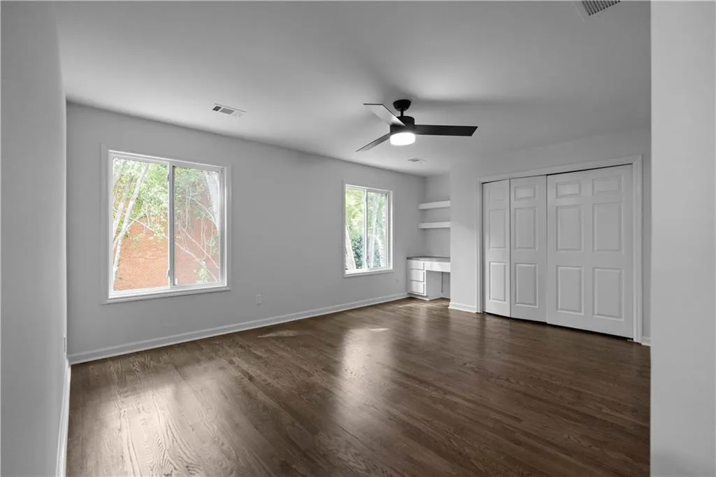 Unfurnished bedroom featuring dark hardwood / wood-style floors, ceiling fan, multiple windows, and a closet