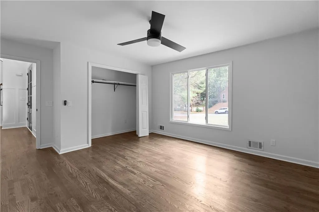 Unfurnished bedroom with a barn door, ceiling fan, a closet, and dark hardwood / wood-style flooring