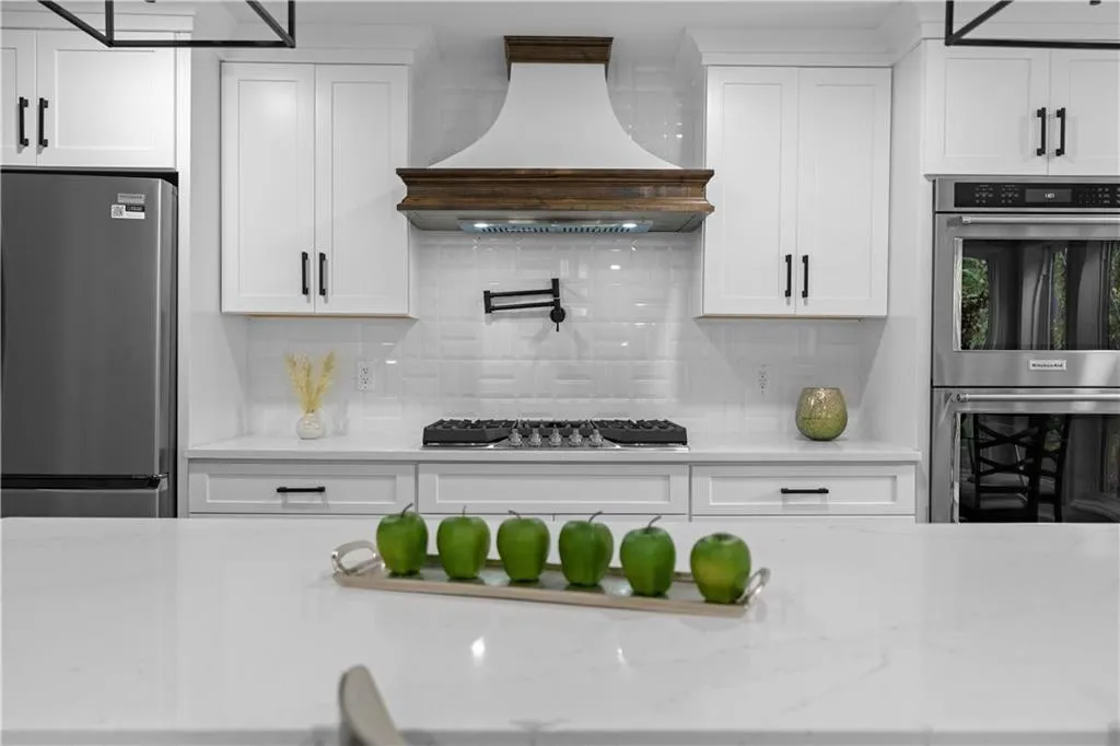 Kitchen with white cabinetry, custom range hood, stainless steel appliances, and light stone counters