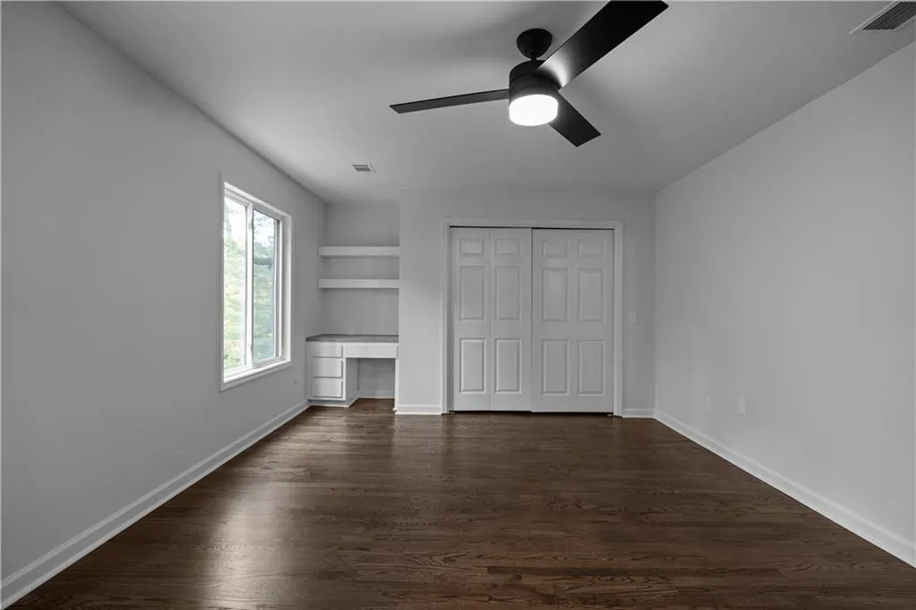 Unfurnished bedroom featuring dark wood-type flooring, a closet, built in desk, and ceiling fan