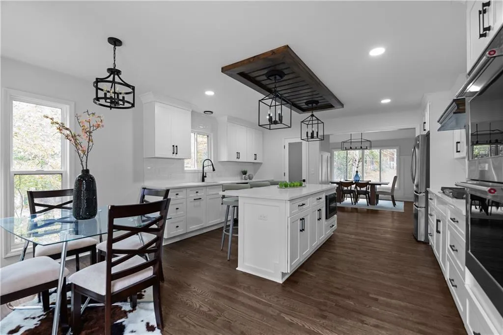 Kitchen with appliances with stainless steel finishes, an inviting chandelier, a kitchen island, white cabinets, and dark wood-type flooring