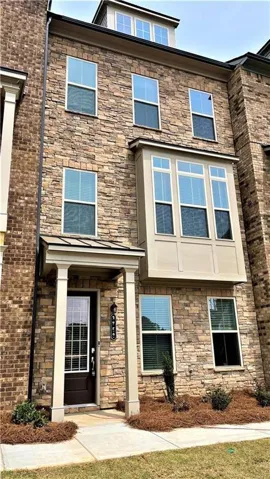 Stone veneer facade with a covered entry, transom window, bay window, and attic dormer